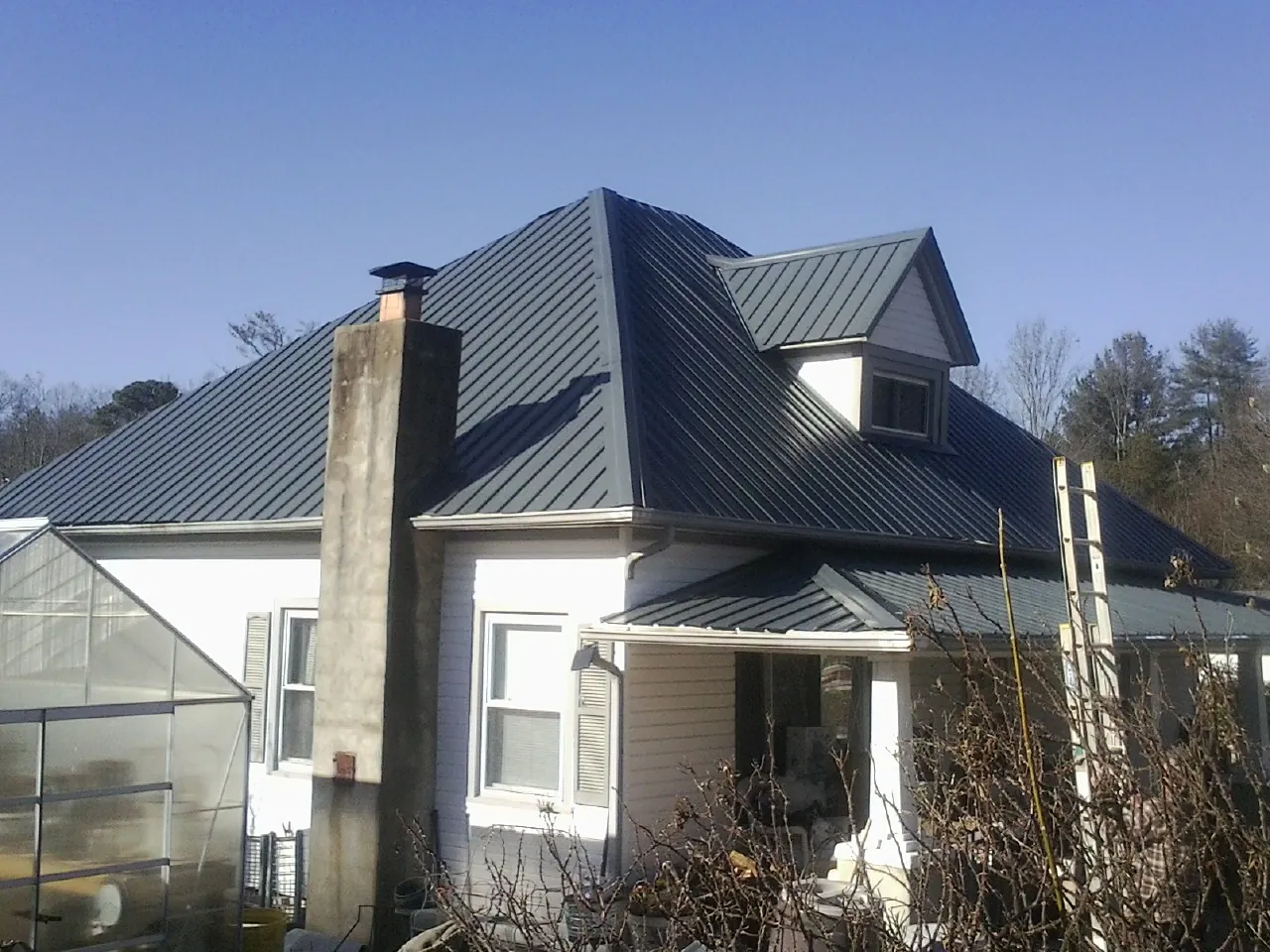Dark blue standing seam metal roof on a white farmhouse with dormer — Slate & Tile Roof Repair by Roofing Brothers in Lignum
