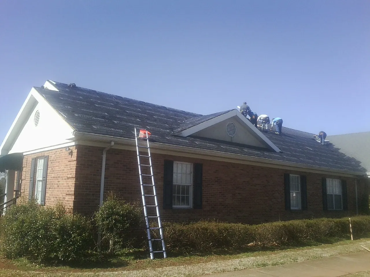 Crew tearing shingles off a brick ranch roof with a ladder set — Metal Roof Repair work by our crew in Lignum