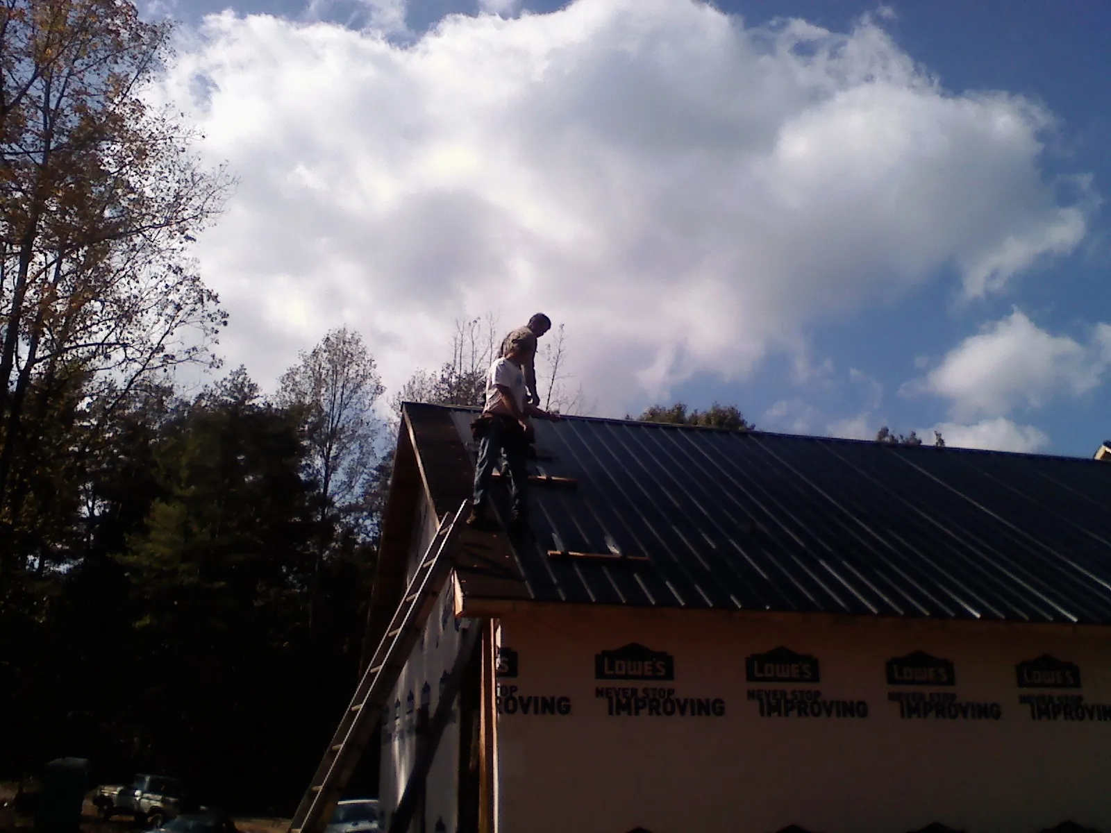 Roofer fastening dark metal panels high against a cloudy sky, from a Roof Inspection job in Lignum