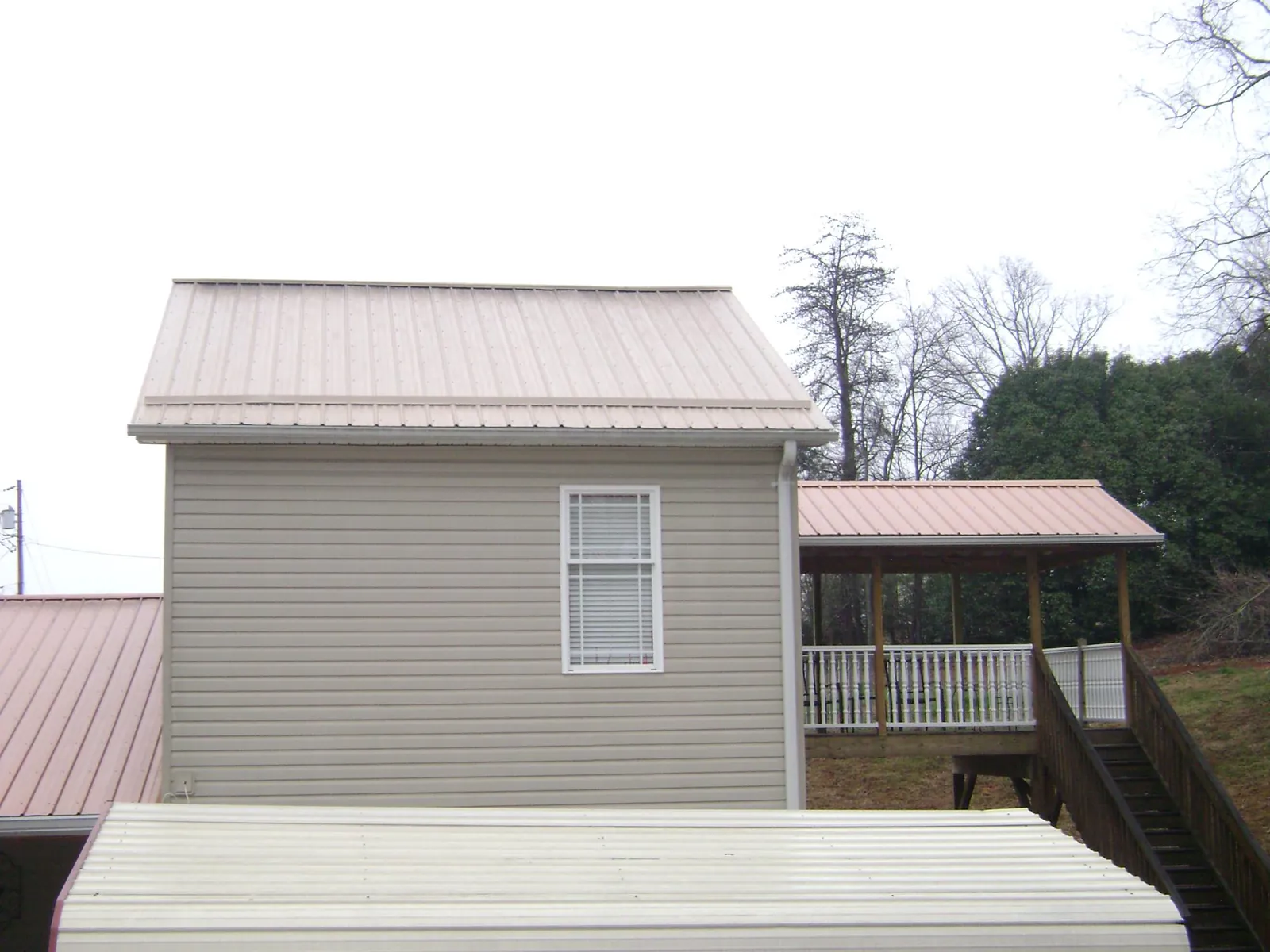 Tan metal roofs on a two story addition and attached porch, from a Roof Replacement job in Lignum